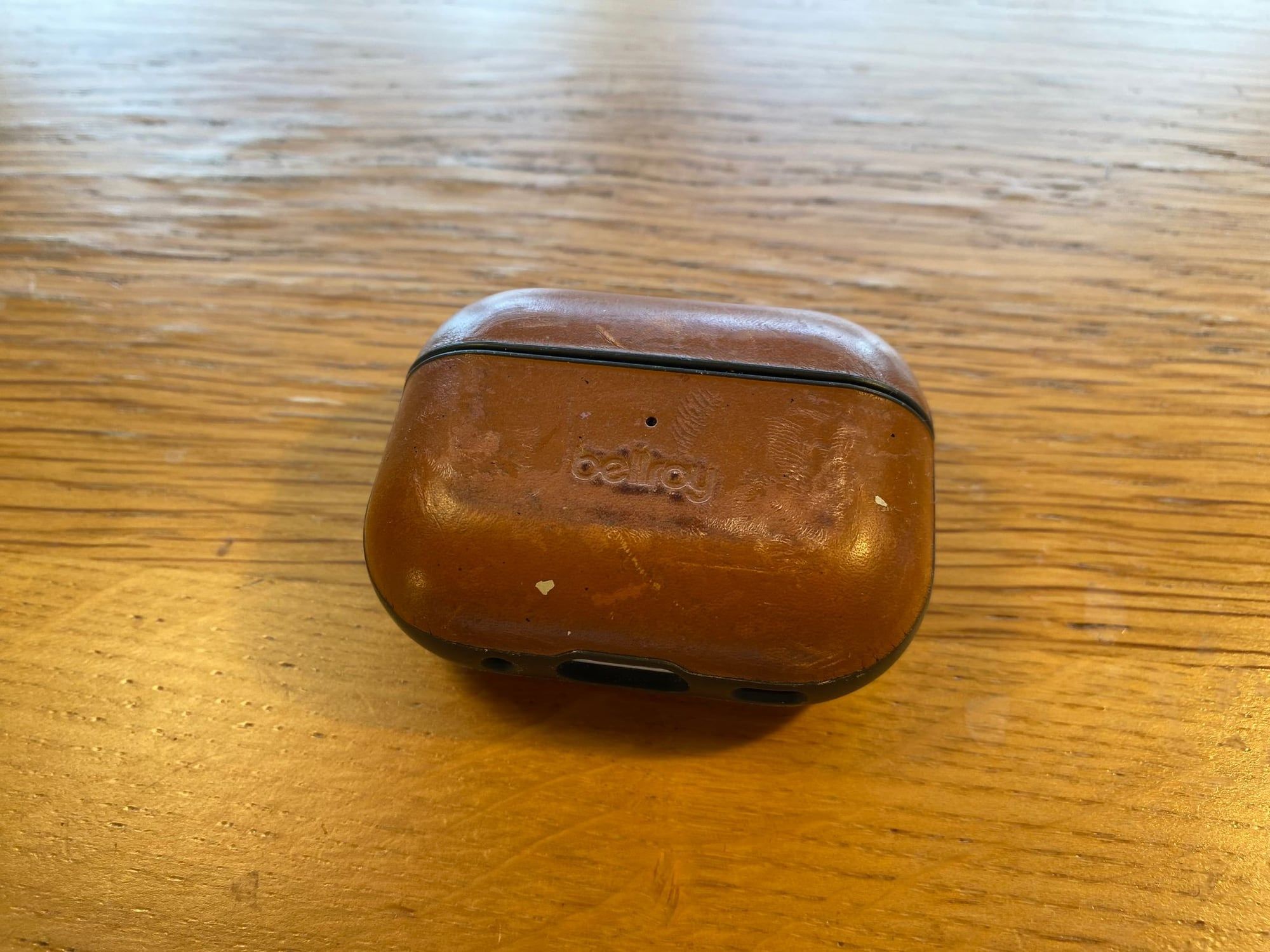 Bellroy leather AirPods Pro case in caramel, on a wooden desk